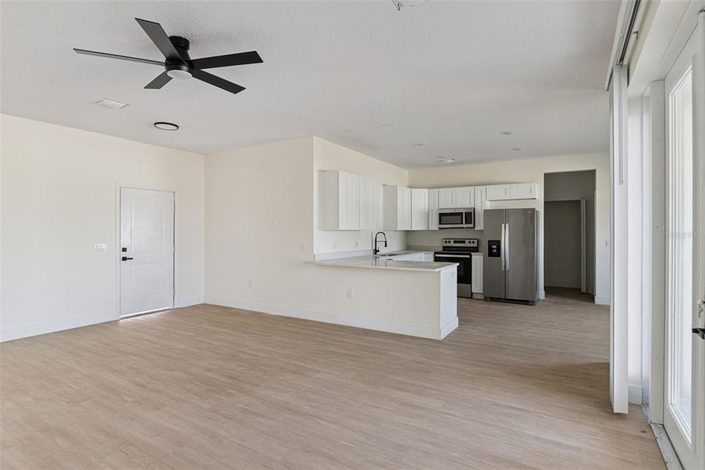 An open-concept kitchen and living area with white cabinets, stainless steel appliances, and wood-look flooring — 1201 APOPKA LANE, KISSIMMEE, FL