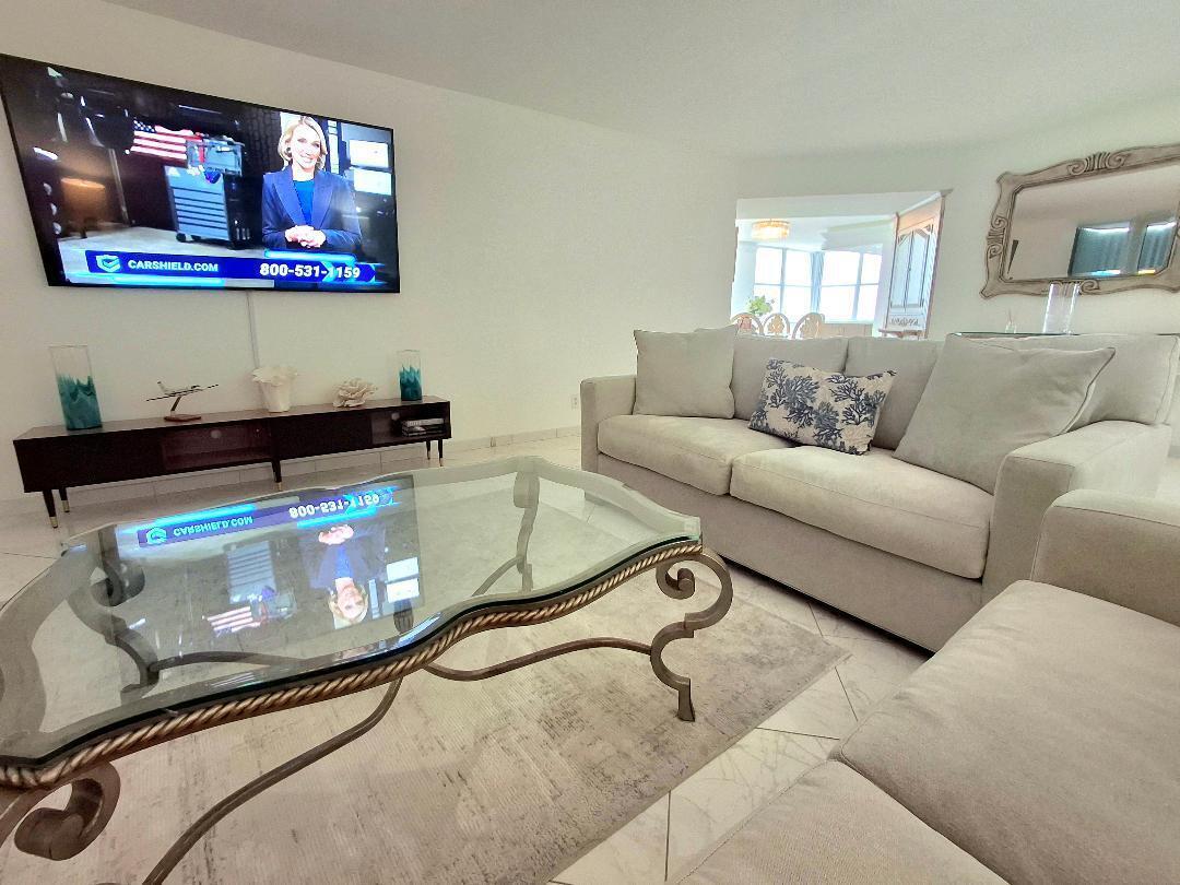 A living room features a wall-mounted television, a glass coffee table, and a light-colored sofa — 1340 S Ocean Boulevard # 1808, Pompano Beach FL 33062, POMPANO BEACH, FL