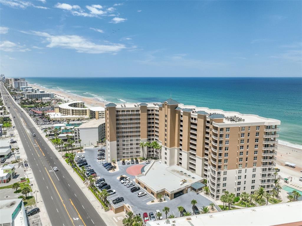 An aerial view shows a large beachfront condominium complex with a parking lot and road — 2403 S ATLANTIC AVENUE UNIT 1008, DAYTONA BEACH SHORES, FL