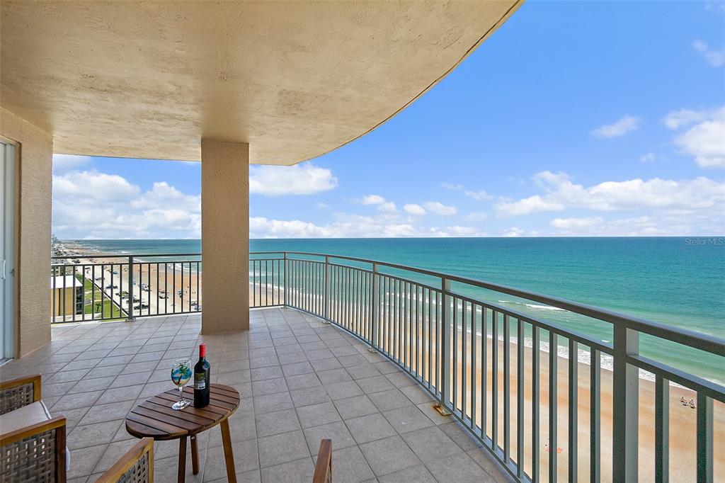 A tiled balcony overlooks the ocean with a small table, wine bottle, and glass — 2403 S ATLANTIC AVENUE UNIT 1008, DAYTONA BEACH SHORES, FL