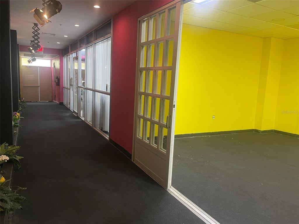 A hallway with black carpet and pink walls leads to a room with yellow walls — 1 C. ISABEL MUÑOZ RIVERA, PONCE, PR