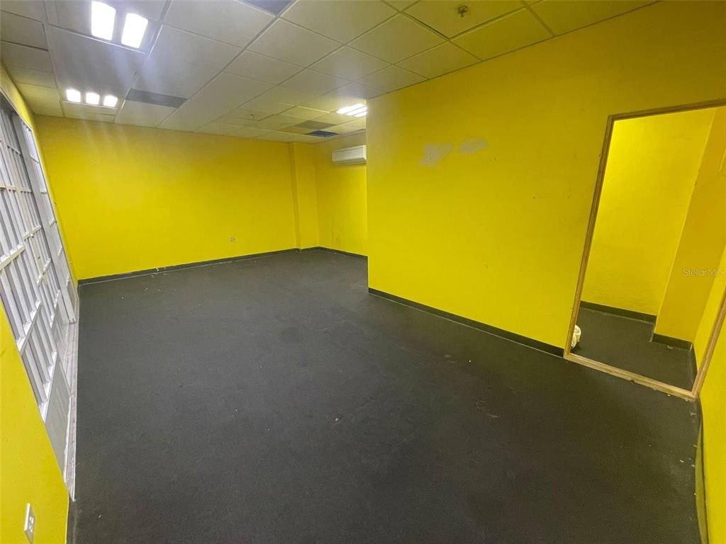 An empty room features bright yellow walls, a dark floor, and a drop ceiling — 1 C. ISABEL MUÑOZ RIVERA, PONCE, PR