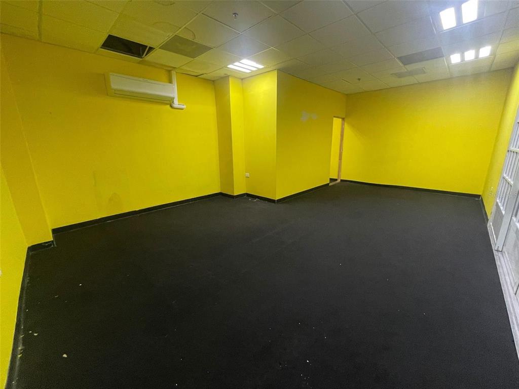 An empty room features bright yellow walls, black carpeting, and a drop ceiling with lights — 1 C. ISABEL MUÑOZ RIVERA, PONCE, PR