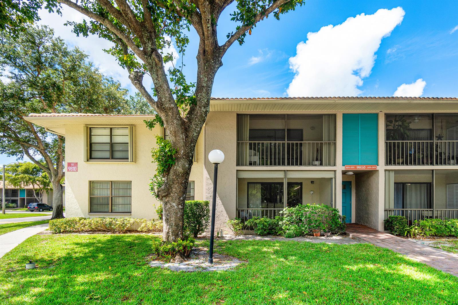 A two-story apartment building with a large tree, screened balconies, and a grassy lawn — 9810 Pineapple Tree Drive # 101, Boynton Beach FL 33436, BOYNTON BEACH, FL