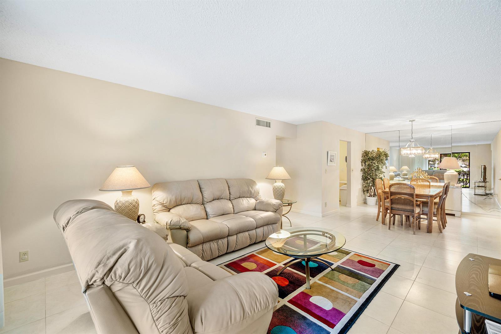 A living room with beige sofas, a colorful area rug, and an adjacent dining area — 9810 Pineapple Tree Drive # 101, Boynton Beach FL 33436, BOYNTON BEACH, FL
