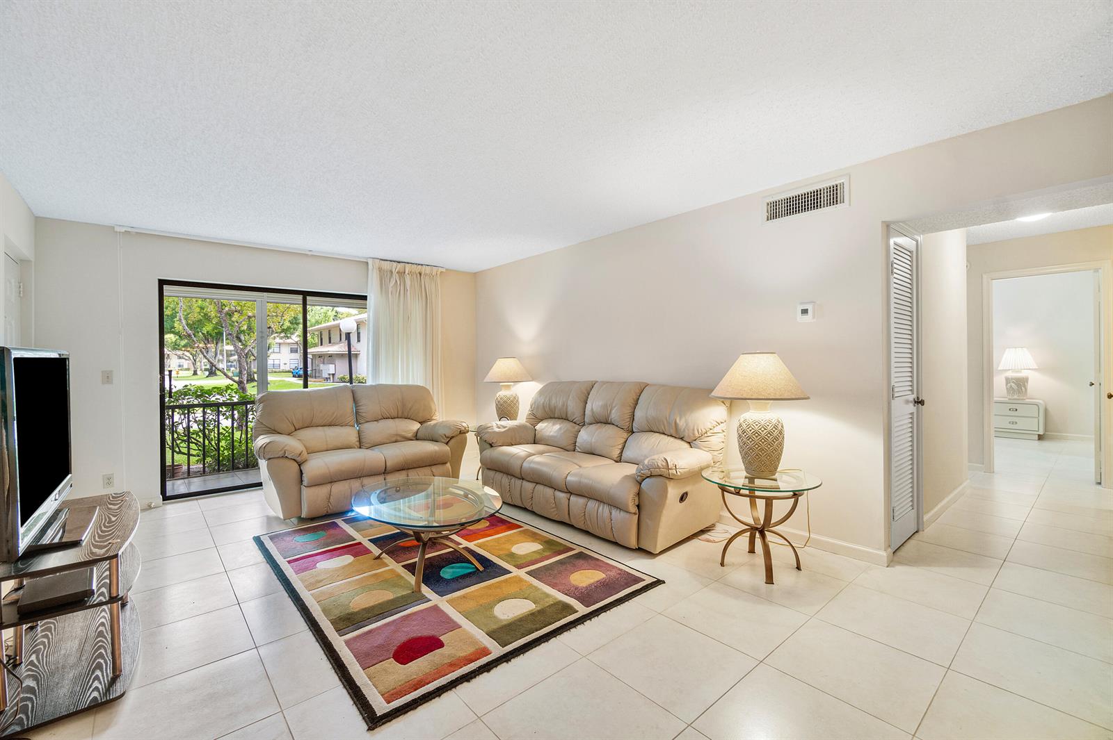 A living room features tile flooring, two beige sofas, a glass coffee table, and a rug — 9810 Pineapple Tree Drive # 101, Boynton Beach FL 33436, BOYNTON BEACH, FL