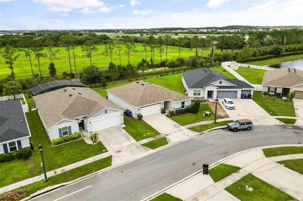An aerial view shows three suburban houses with driveways and lawns bordering a grassy field — 3140 SWEET ACRES PLACE, ST CLOUD, FL
