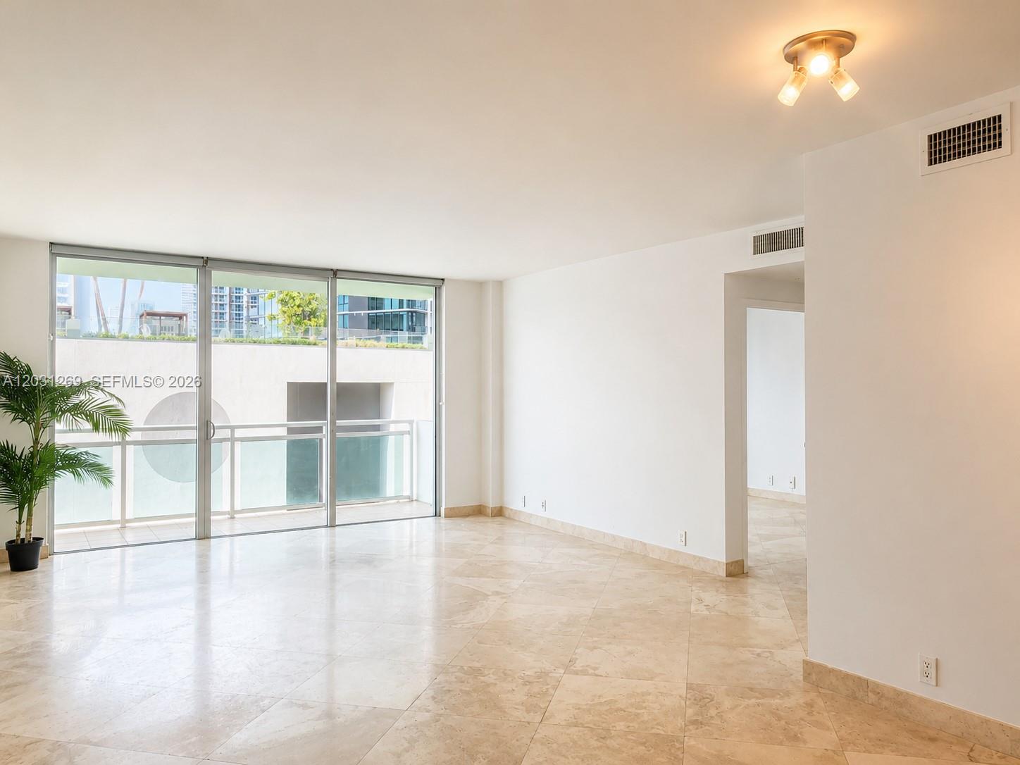 An empty living room features beige tile flooring, white walls, and sliding glass balcony doors — 3301 NE 5th Ave # 908, Miami FL 33137, MIAMI, FL