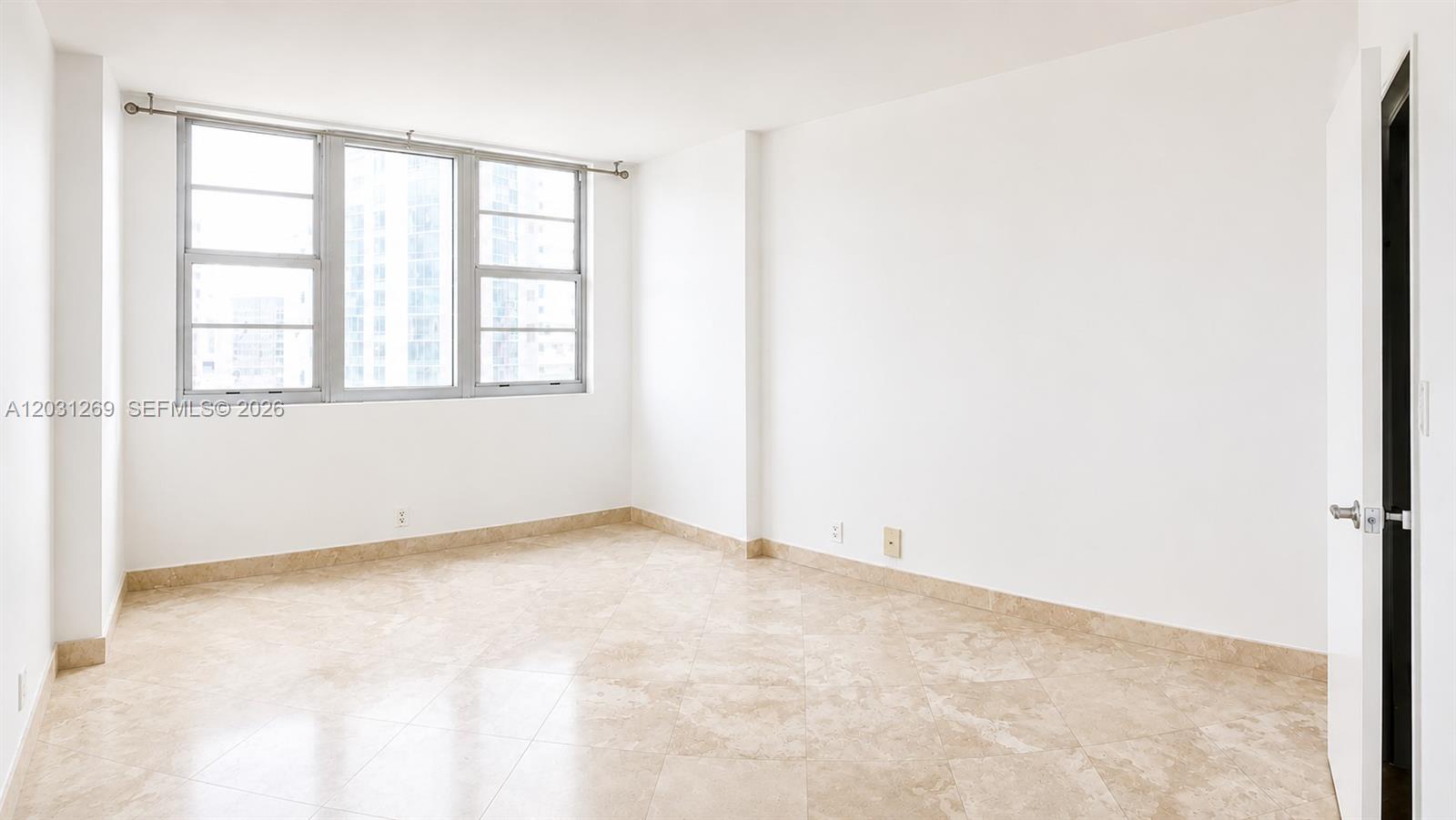 An empty room features white walls, beige tile flooring, and a large window with city views — 3301 NE 5th Ave # 908, Miami FL 33137, MIAMI, FL