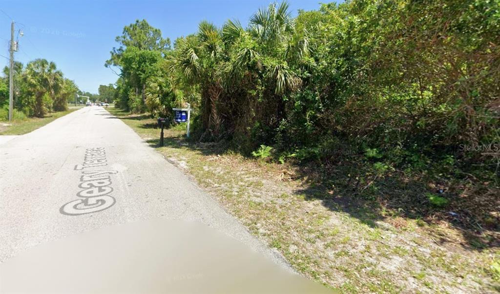 A paved road runs alongside a vacant, heavily wooded lot with a real estate sign — Lot 11 GEARY TERRACE, NORTH PORT, FL