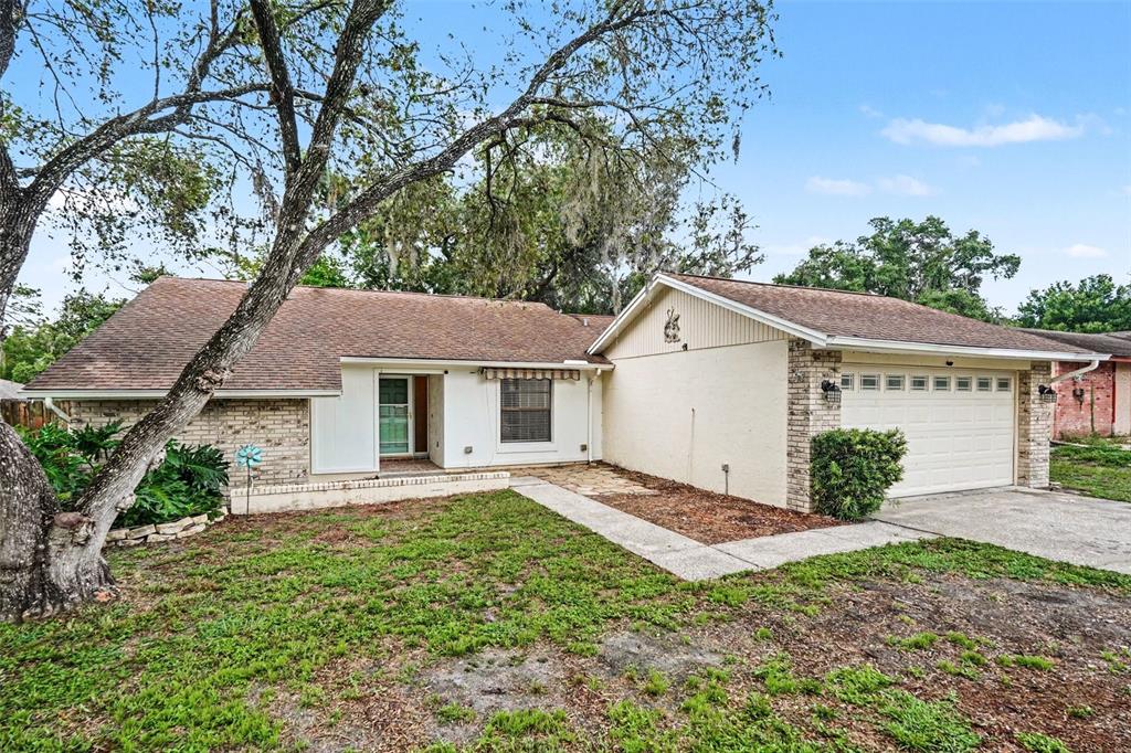 A single-story house with a brick and stucco exterior, a garage, and a large tree — 17703 CRANBROOK DRIVE, LUTZ, FL