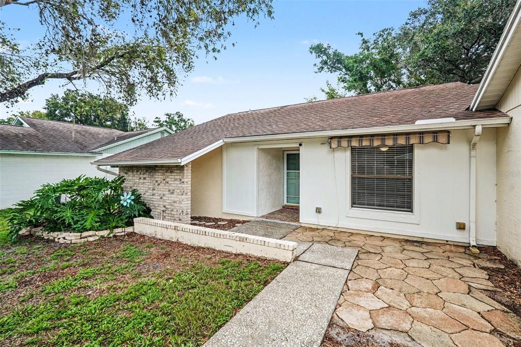 The exterior of a single-story house features a stone patio, brick accents, and a walkway — 17703 CRANBROOK DRIVE, LUTZ, FL
