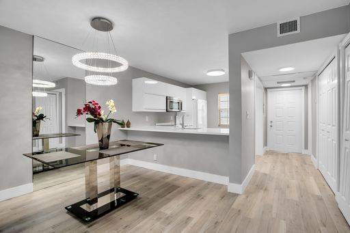 A modern dining area with a glass table and chandelier opens to a white kitchen — 3503 Oaks Way # 303, Pompano Beach FL 33069, POMPANO BEACH, FL