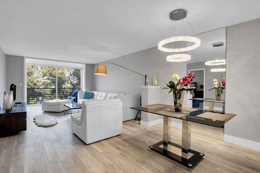 A modern living and dining room features light wood floors, white furniture, and a chandelier — 3503 Oaks Way # 303, Pompano Beach FL 33069, POMPANO BEACH, FL
