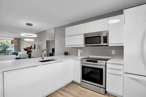 A modern kitchen features white cabinetry, stainless steel appliances, and a white countertop — 3503 Oaks Way # 303, Pompano Beach FL 33069, POMPANO BEACH, FL