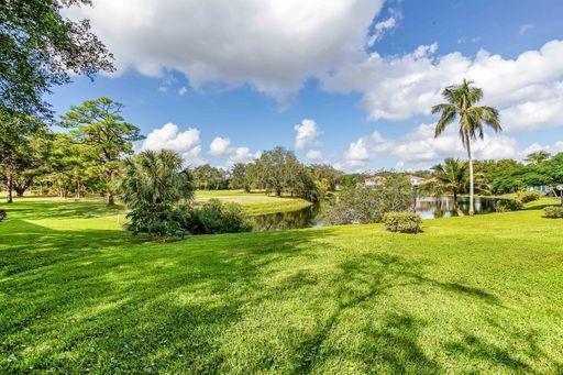 A grassy lawn leads to a small pond surrounded by trees and a palm tree — 3503 Oaks Way # 303, Pompano Beach FL 33069, POMPANO BEACH, FL