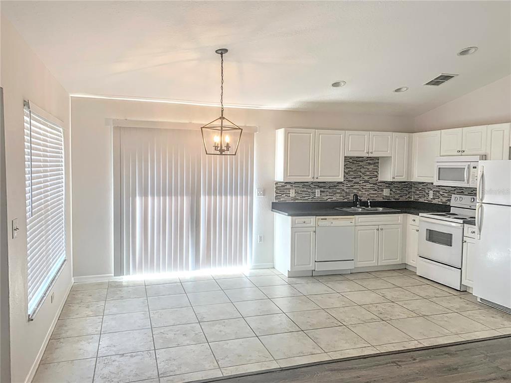 A kitchen and dining area with white cabinets, tile flooring, and a hanging light fixture — 5440 KENSINGTON STREET, SARASOTA, FL