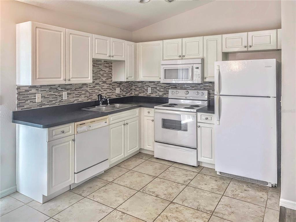 A kitchen with white cabinets, dark countertops, a tiled backsplash, and white appliances — 5440 KENSINGTON STREET, SARASOTA, FL