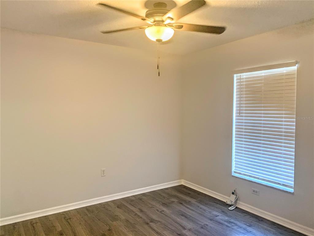 An empty bedroom features light gray walls, wood-look flooring, a ceiling fan, and a window — 5440 KENSINGTON STREET, SARASOTA, FL