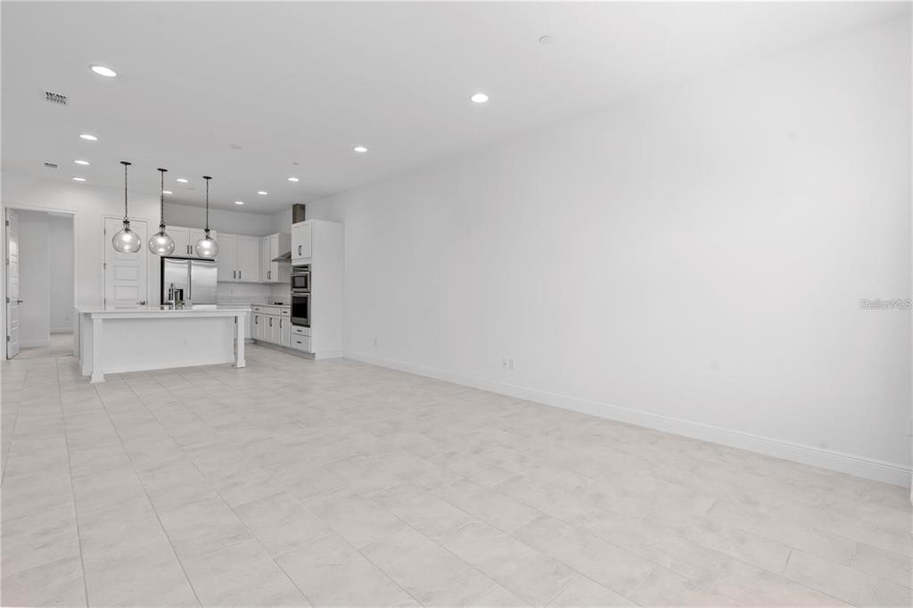 A bright, open-concept kitchen and living area featuring white cabinetry, a center island, and tile flooring — 9832 BUCKLOW HILL DRIVE, ORLANDO, FL