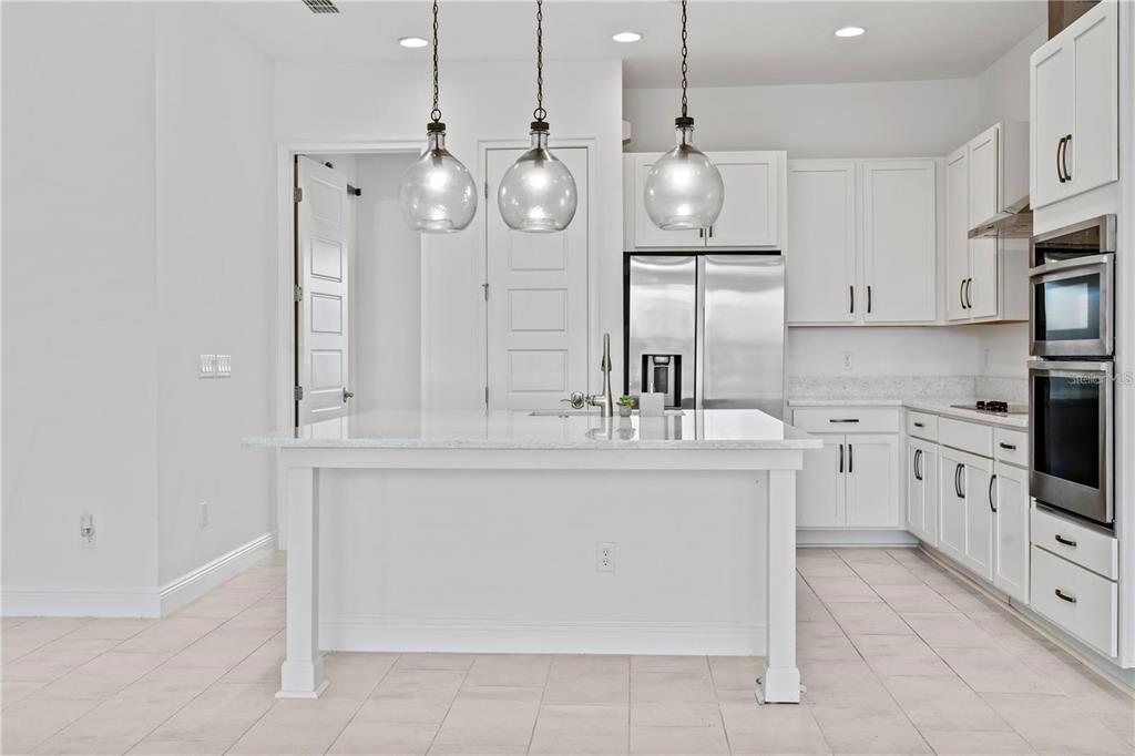 A kitchen with white cabinets, a granite-topped island, stainless steel appliances, and three pendant lights — 9832 BUCKLOW HILL DRIVE, ORLANDO, FL