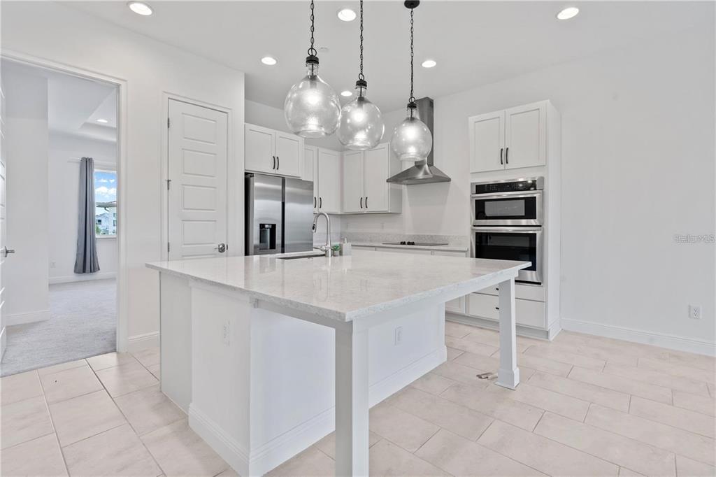 A modern white kitchen features a large island, stainless steel appliances, and three glass pendants — 9832 BUCKLOW HILL DRIVE, ORLANDO, FL