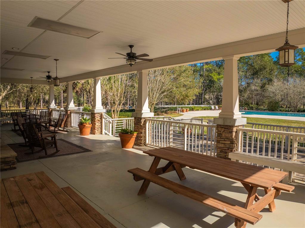 A covered porch features wooden picnic tables, rocking chairs, and a view of a swimming pool — 1680 SW 188TH STREET, NEWBERRY, FL