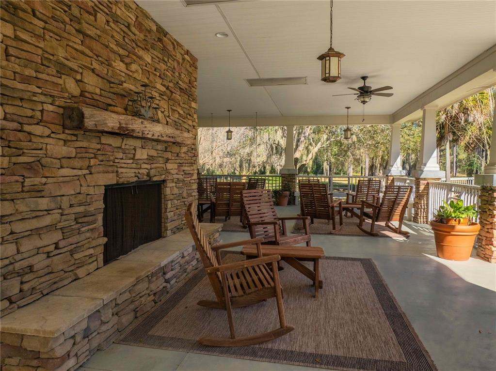 A covered stone patio features a large fireplace, several wooden rocking chairs, and outdoor lighting — 1680 SW 188TH STREET, NEWBERRY, FL