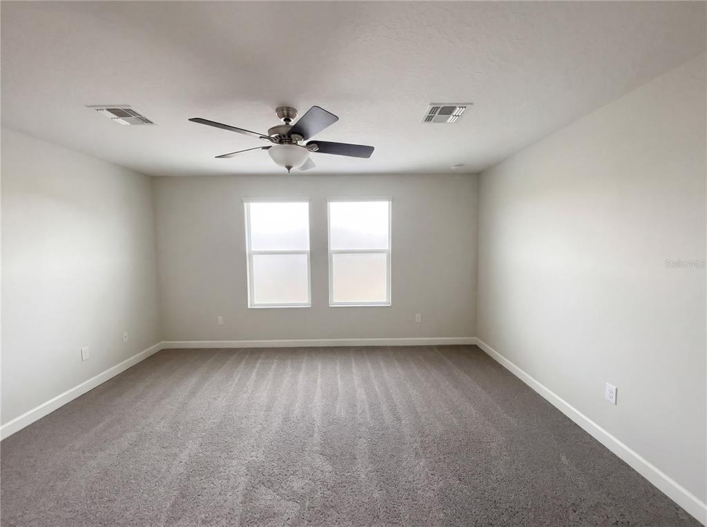 An empty bedroom features gray carpeting, light-colored walls, a ceiling fan, and two windows — 11072 SILVER SURFER ALLEY, WINTER GARDEN, FL