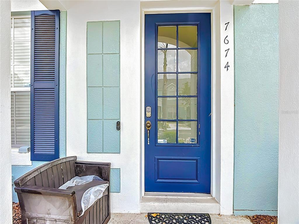 A blue front door with glass panes sits next to a bench and light-colored siding — 7674 OTTERSPOOL STREET, KISSIMMEE, FL