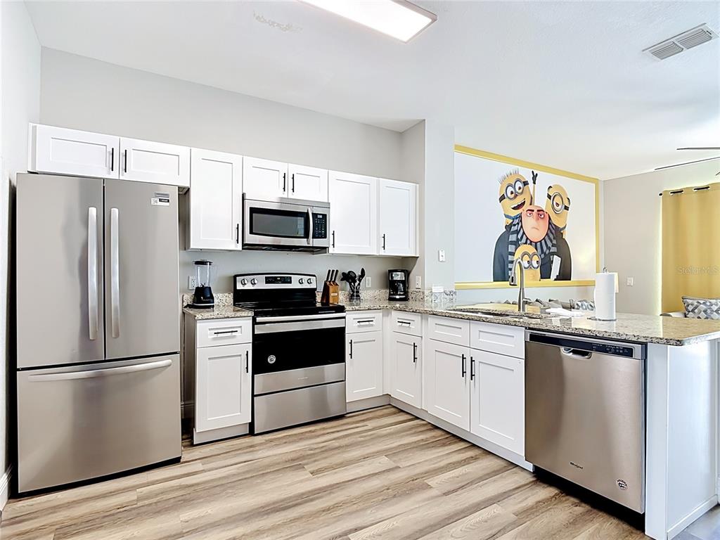 A kitchen features white cabinets, stainless steel appliances, granite countertops, and a Minion-themed wall mural — 7674 OTTERSPOOL STREET, KISSIMMEE, FL