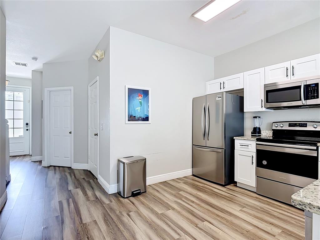 A kitchen features stainless steel appliances, white cabinets, and wood-look flooring — 7674 OTTERSPOOL STREET, KISSIMMEE, FL