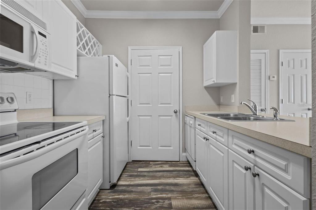 A kitchen features white cabinetry, white appliances, a double sink, and wood-look flooring — 1216 S MISSOURI AVENUE UNIT 116, CLEARWATER, FL