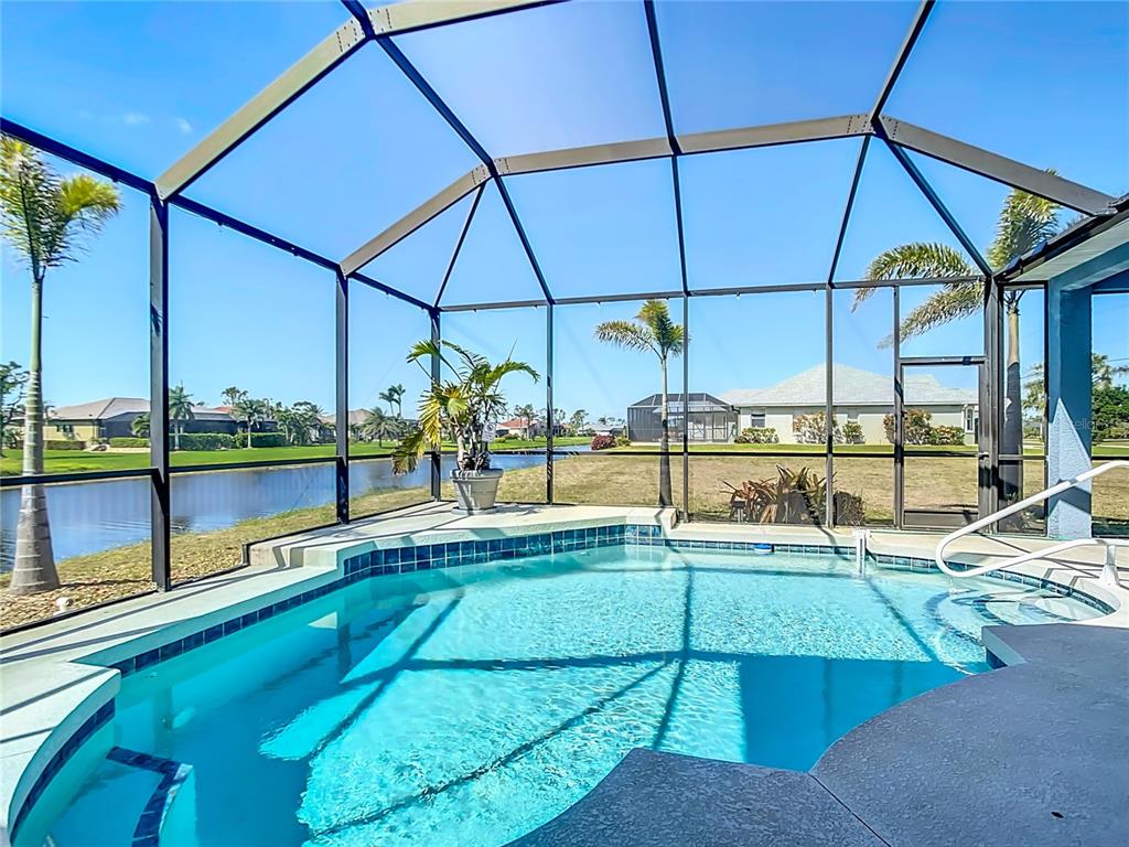 A screened-in swimming pool overlooks a lake and neighboring houses on a sunny day — 1167 ROTONDA CIRCLE, ROTONDA WEST, FL