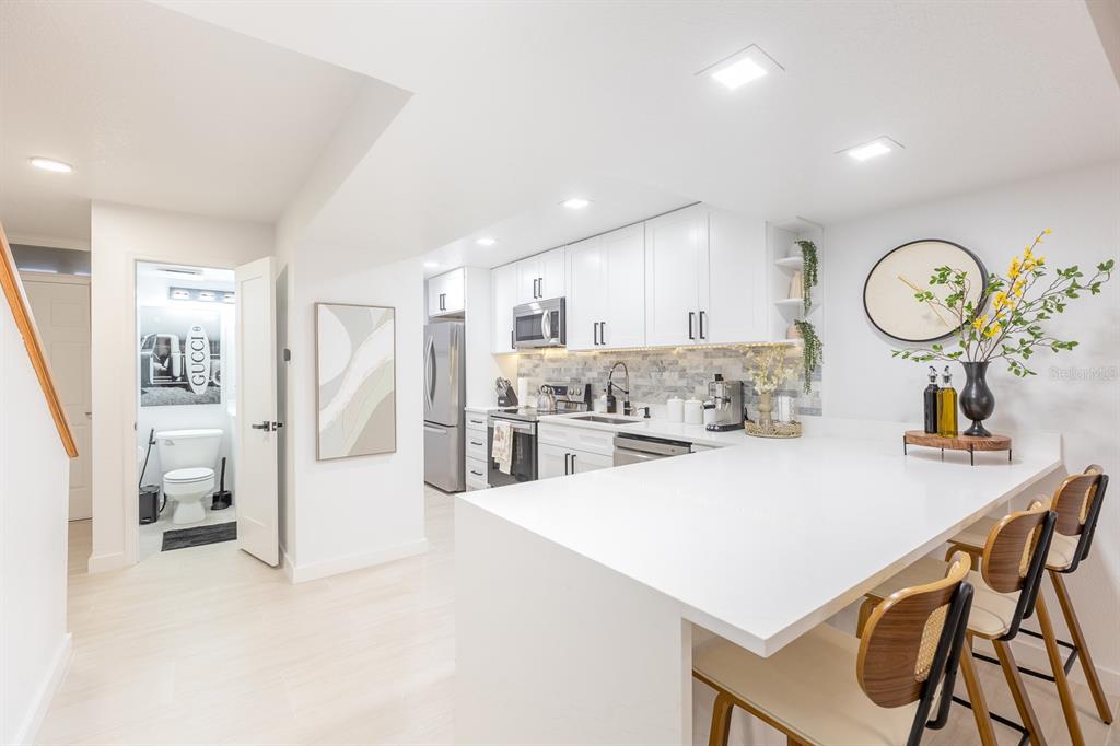 A modern white kitchen features a breakfast bar, stainless steel appliances, and an adjacent bathroom — 701 S ATLANTIC AVENUE UNIT UT21, NEW SMYRNA BEACH, FL