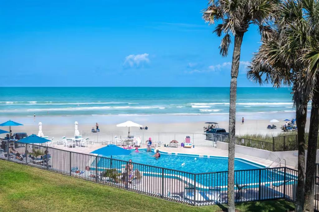 A swimming pool with lounge chairs sits behind a fence overlooking a sandy beach — 701 S ATLANTIC AVENUE UNIT UT21, NEW SMYRNA BEACH, FL
