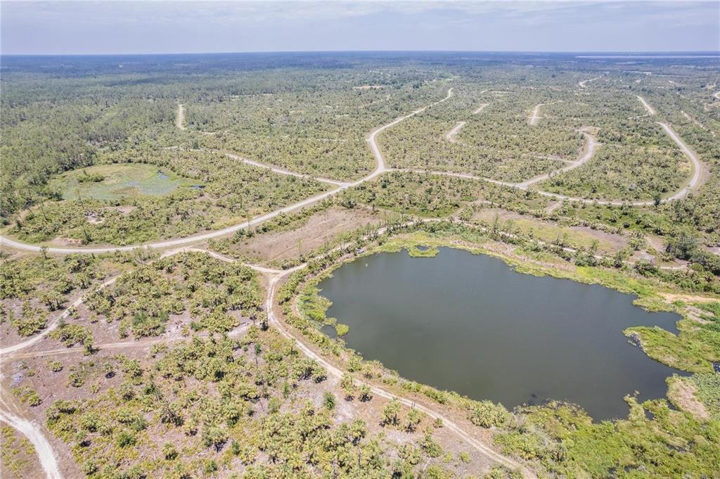 An aerial view shows a large pond surrounded by undeveloped land with dirt roads — KIMBERLY DRIVE, NORTH PORT, FL
