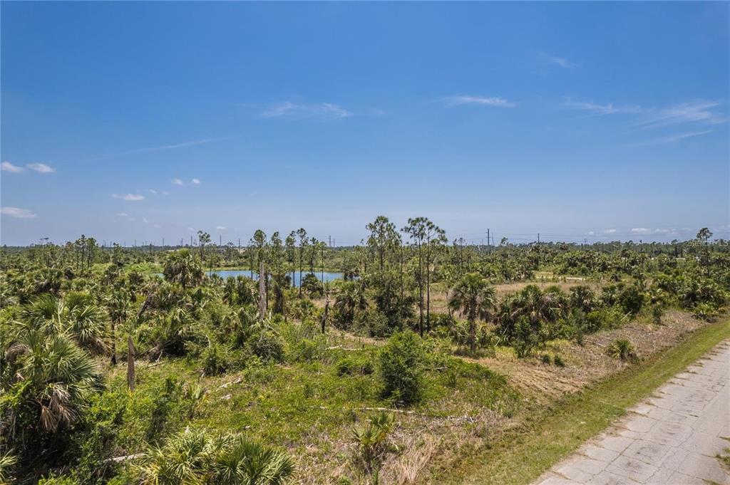 An elevated view of a grassy, wooded lot with a small pond under a blue sky — KIMBERLY DRIVE, NORTH PORT, FL