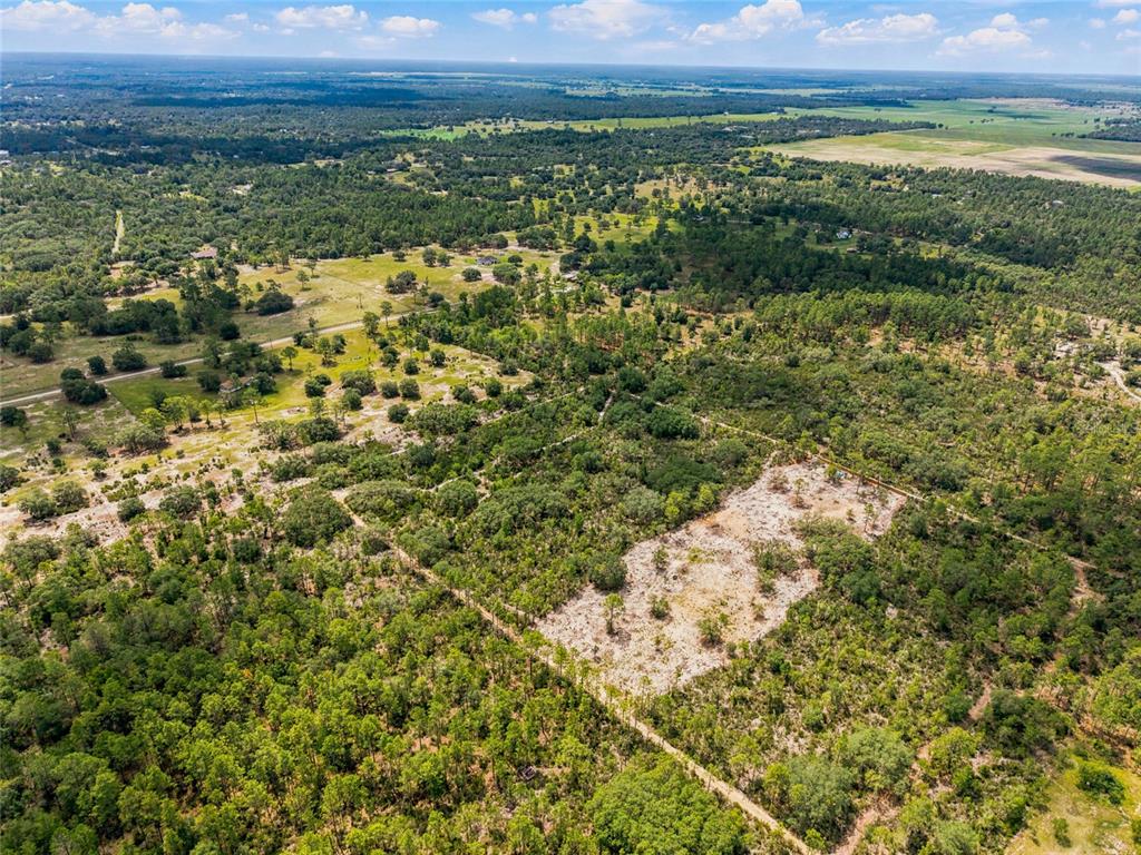 An aerial view shows a large, partially cleared plot of land surrounded by dense forest — Lot 00 NE 56TH ST, BRONSON, FL