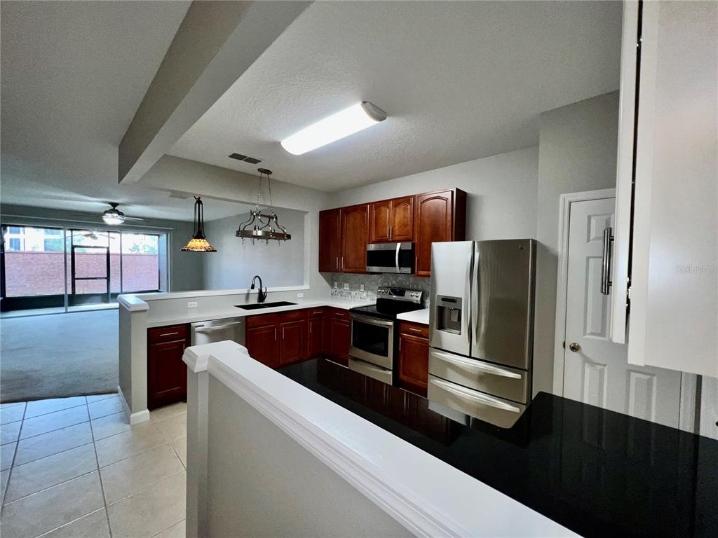 A kitchen features dark wood cabinets, stainless steel appliances, and black countertops — 2648 GALLIANO CIRCLE, WINTER PARK, FL