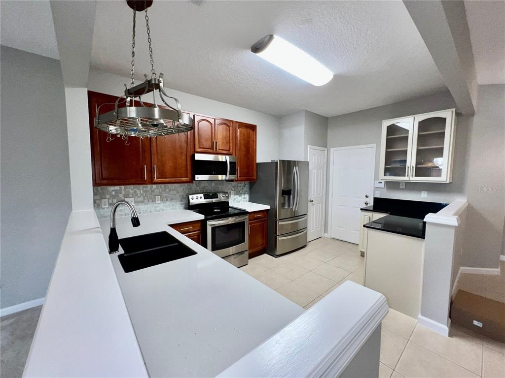 A kitchen features wood cabinets, stainless steel appliances, a white countertop, and a hanging rack — 2648 GALLIANO CIRCLE, WINTER PARK, FL