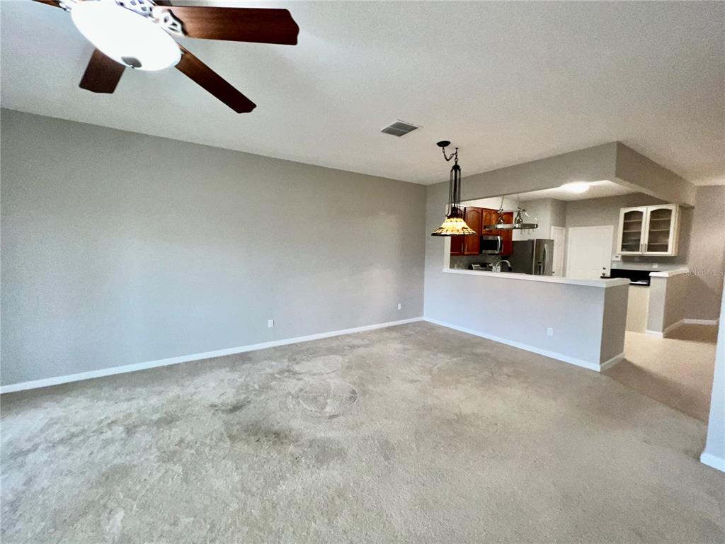 An open-concept living room features beige carpeting, a ceiling fan, and a kitchen pass-through — 2648 GALLIANO CIRCLE, WINTER PARK, FL
