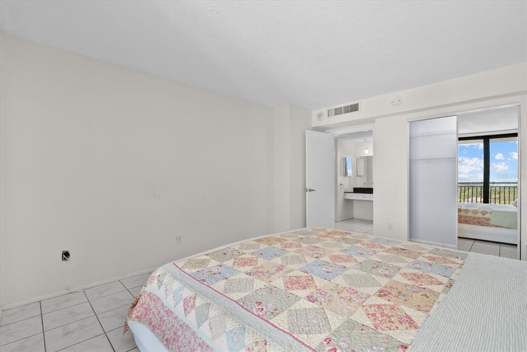 A bedroom features a white bed with a patterned quilt, tile flooring, and a sliding glass door — 4822 OCEAN BOULEVARD UNIT 11E, SARASOTA, FL