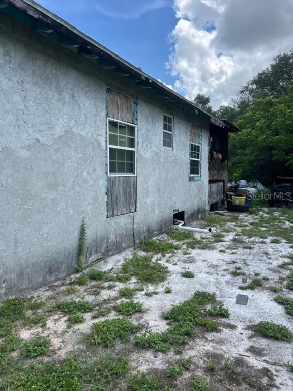 The exterior of a house shows stucco walls, boarded-up windows, and fire damage — 108 PLANTATION LANE, WAVERLY, FL
