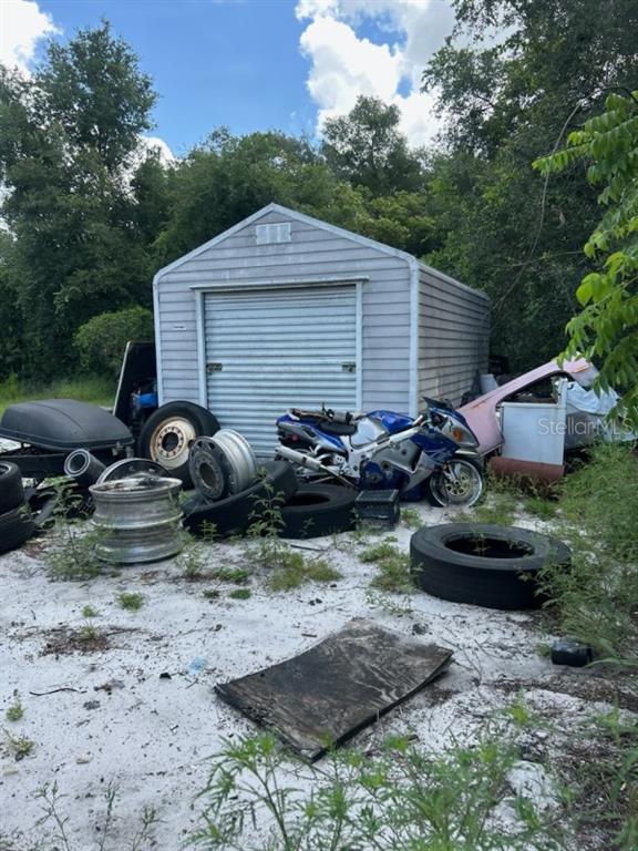 A detached metal storage shed sits in a yard cluttered with tires and a motorcycle — 108 PLANTATION LANE, WAVERLY, FL