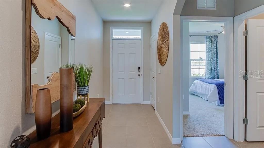 A hallway features a wooden console table, a mirror, and a doorway leading to a bedroom — 17214 HARVEST MOON WAY, BRADENTON, FL
