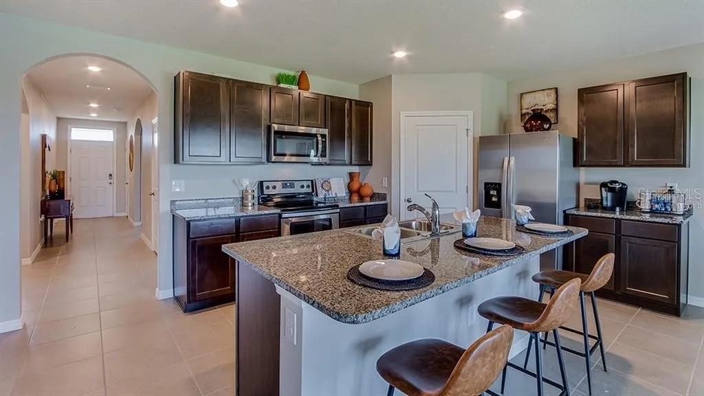 A kitchen features dark wood cabinets, granite countertops, a central island, and stainless steel appliances — 17214 HARVEST MOON WAY, BRADENTON, FL