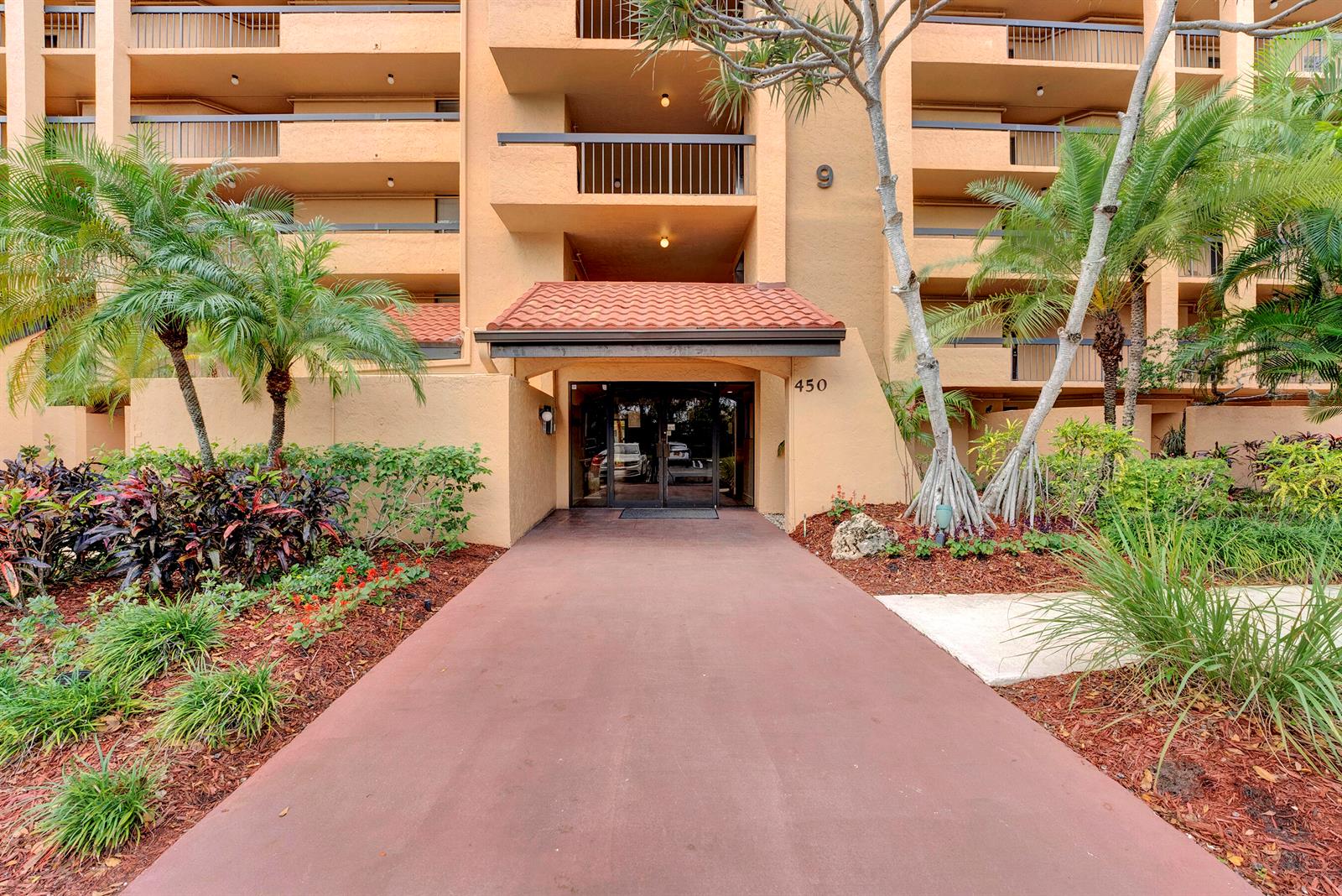 The exterior of a multi-story apartment building features a covered entrance with the number 450 — 450 Egret Circle # 9202, Delray Beach FL 33444, DELRAY BEACH, FL