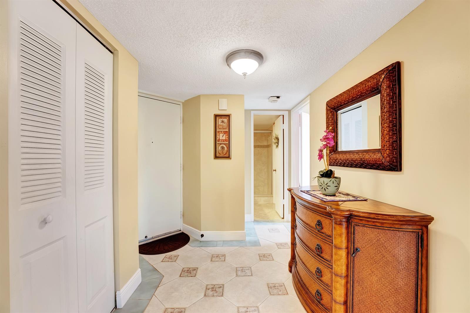 A hallway features tile flooring, a wooden dresser with a mirror, and a white closet — 450 Egret Circle # 9202, Delray Beach FL 33444, DELRAY BEACH, FL