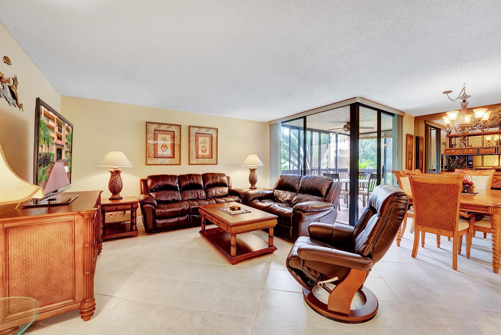 A living room with brown leather furniture, a television, and an adjacent dining area — 450 Egret Circle # 9202, Delray Beach FL 33444, DELRAY BEACH, FL